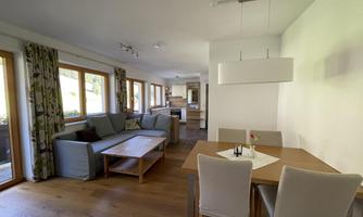 A cozy living space with bright windows and modern furniture. The room includes a dining area and a comfortable sitting area.
