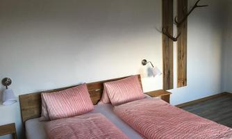 A bright bedroom with two single beds and a wooden design. On the wall, there is a decorative element made of wood and a couple of lamps.