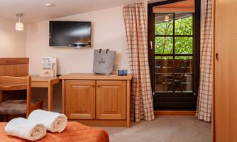 A cozy room with a television and a table. The windows lead to a balcony overlooking greenery.