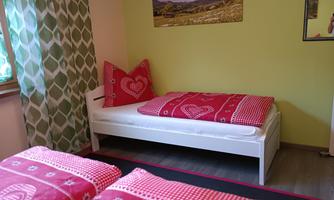 A cozy bedroom with a white bed and red bedcovers. The walls are painted in a fresh yellow tone, and a picture hangs above the bed.