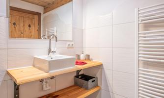 A modern bathroom with a sink on a wooden shelf. The walls are brightly tiled, and a towel rack is visible.