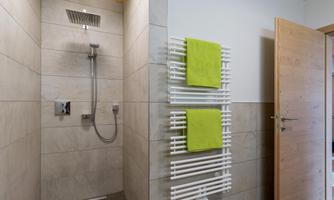 A modern bathroom with a walk-in shower and a warm atmosphere. Green towels hang on a white towel warmer.