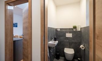 A modern bathroom with a toilet and a small sink. The walls are made of dark stone and the atmosphere is bright and clean.
