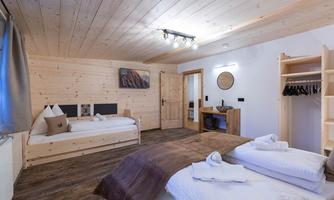 A modern room with wooden walls and a light wooden floor. There are two beds, a cozy seating area, and a wardrobe.