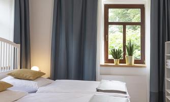A bright bedroom with two beds and fresh plants by the window. The curtains are dark blue and create a cozy look.