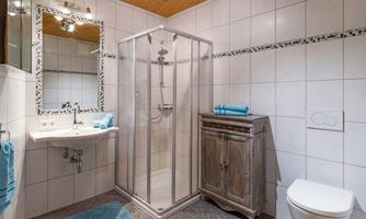 A modern bathroom with a shower cabin and a sink. The walls are tiled, and there is a wooden ceiling as well as decorative towels in turquoise.