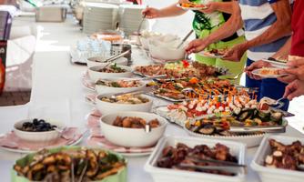 A lavish buffet with various dishes, including seafood and appetizers. People are serving themselves at a long table.