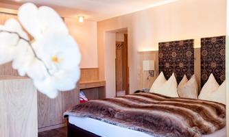 A cozy bedroom with a large bed and elegant decor. In the foreground, an orchid blooms, giving the room a special touch.