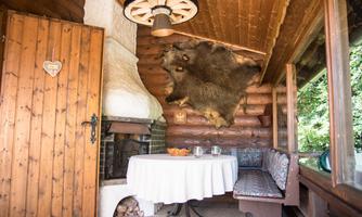 A cozy room with wood paneling and a round table. An animal hide hangs on the wall, and a fireplace creates a rustic atmosphere.