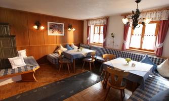 A cozy dining area with wooden walls and various seating options. The room is pleasantly lit and has large windows with curtains.