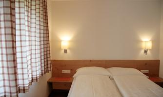 A cozy room with two single beds and soft light. The windows are adorned with checked curtains.