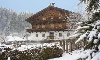 A traditional wooden house in the snow, surrounded by a wintry landscape. The trees are covered with a layer of snow and the atmosphere is calm and peaceful.
