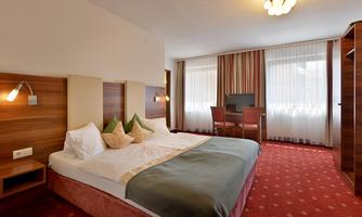 A modern hotel room with a double bed and bright curtains. The room features a desk and a television.