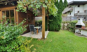 A cozy outdoor area with a wooden terrace and two chairs. In the background, a grill and green plants can be seen.