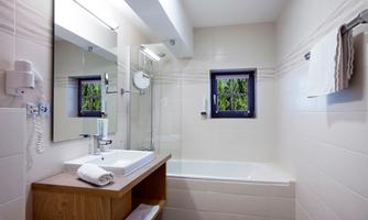 A modern bathroom with a bathtub and a sink. There is a mirror and a small window overlooking greenery.