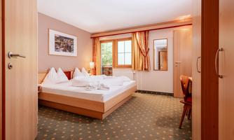 A cozy room with a double bed and bright textiles. The room has a window overlooking the outside and is harmoniously furnished.
