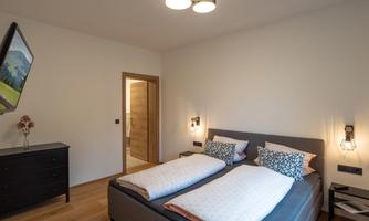 A modern bedroom with a double bed and two nightstands. The walls are light and the floor is made of wood.