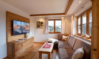 A cozy living room with wood paneling and a large window. There is a sofa, a coffee table, and a television.