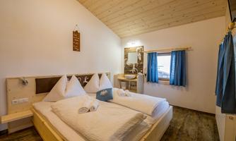 A cozy bedroom with two beds and white bed covers. Large windows provide plenty of daylight and a pleasant atmosphere.