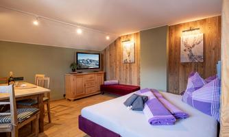 A cozy room with a double bed, a dining table, and a television. The walls are partially made of wood, and there are decorative pictures.