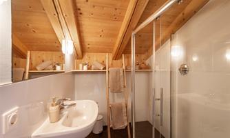 A modern bathroom with wooden beams and a shower. There is a sink and towels that are neatly stored.