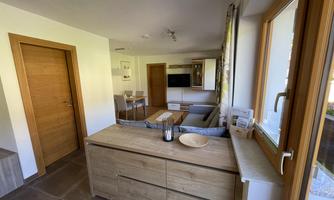 A modern, bright living kitchen with wooden details and a cozy ambiance. The room is well-lit and provides a living area with a sofa, a table, and a TV corner.