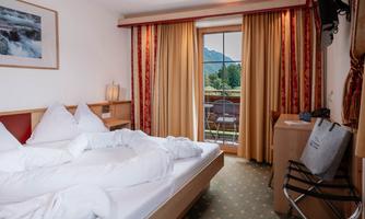 A cozy hotel room with a large bed and fresh bed linen. There is a balcony with a view of the mountains and soft curtains.