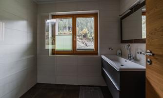 A modern bathroom with a large window that offers a view of trees. The decor is bright and simple, featuring an elegant sink and a mirror.