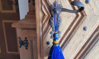 A decorative metal hook on a wooden door. The hook is adorned with a blue tassel.