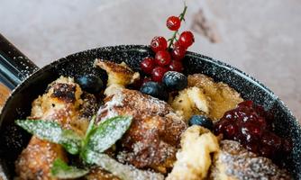 An appetizing pan with baked bread, garnished with berries and a touch of powdered sugar. Fresh mint and red currants complement the dish.