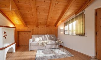 A cozy living room with a wooden ceiling and a bright sofa. A small table and a rug complement the inviting atmosphere.