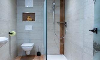 A modern bathroom with a shower and toilet. The walls are light, and the floor has a warm tone.