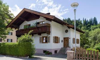 A charming house in alpine style with a wooden balcony and blooming plants. Surrounded by trees and a quiet residential street.