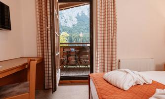 A cozy room with a bed and a table. From the balcony, there is a view of the mountains and nature.