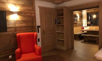 A cozy room with a red armchair and wooden walls. On the right side, another living area with a table and additional seating is visible.