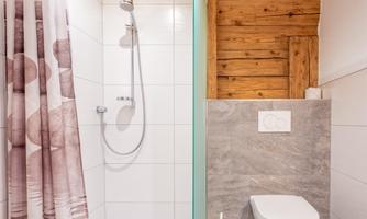 A modern bathroom with a shower and a toilet. The wall is partially clad with wood, while the shower is done in a light tile style.