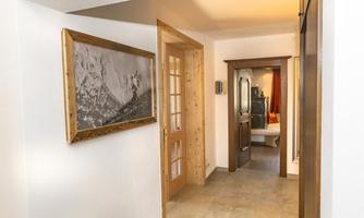 A bright hallway with a wooden door frame and a photo on the wall. In the background, another room with a bed is visible.