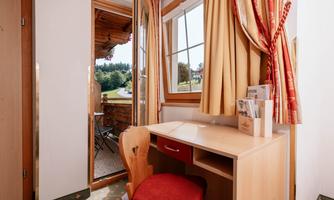 A cozy study with a desk and a red chair. Through the window, the view of a green landscape can be seen.