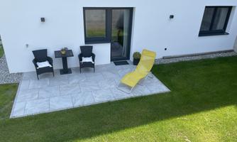 A sunny terrace with two black chairs and a small table. A yellow lounge chair is on the tiled floor.