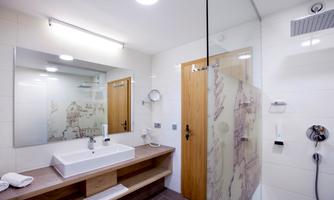 A modern bathroom with a white sink and a large mirror. The shower is separated by a glass wall and the room feels bright and inviting.