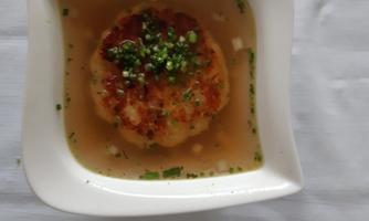 A plate with a golden-brown meatball in clear broth, garnished with fresh herbs. The serving is done in an elegant white bowl.