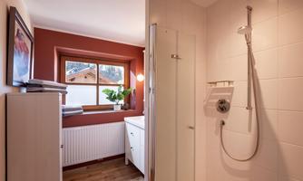 A modern bathroom with a shower cabin and a window. The room has warm colors and wooden flooring.
