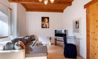 A modern living room with light walls and a wooden ceiling. It is furnished with a gray sofa, a table, and a television.