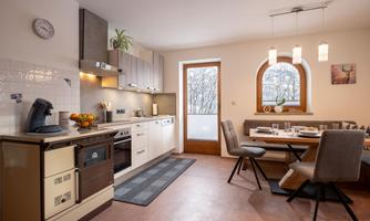 A modern kitchen with a dining area and large windows. The space is brightly and invitingly furnished.