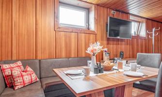 A cozy dining area with wood paneling and a large table. The table is arranged with dishes and a small floral decoration.