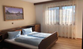 A bright sleeping area with a double bed and blue pillows. Large windows let in plenty of daylight, and the walls are simply designed.