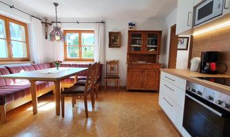 A bright and inviting kitchen with a dining area and large windows. The space has a cozy atmosphere with wood and fabric accents.