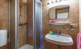 A small bathroom with a shower enclosure and a sink. The walls are tiled in warm shades of brown and beige.