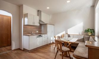 A modern kitchen with bright walls and wooden floors. A dining area with cozy seating and a plant arrangement by the window.