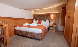 A cozy hotel room with a double bed and wooden paneling. The decor is simple and elegant, with warm colors.